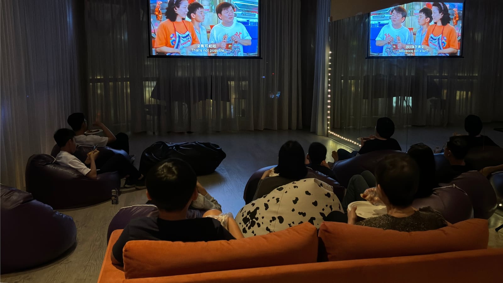 The private cinema — projector screen, sofas and bean bags under ambient lighting